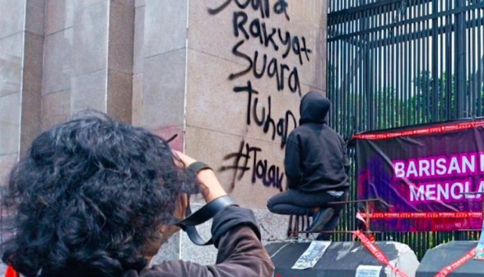 Seorang masa aksi saat menuliskan tuntutan di dinding pagar gedung DPR RI Jakarta, Kamis (20/3/2025). ANTARA/Khaerul Izan